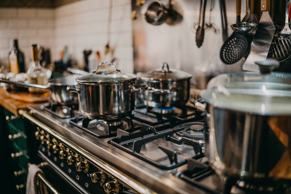 Person using a stainless steel pressure cooker on a kitchen counter with recipe notes nearby